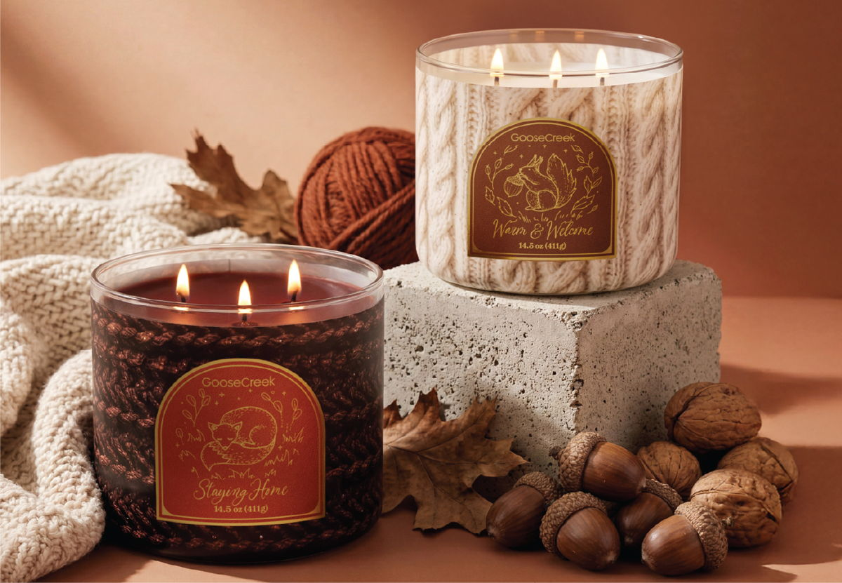 Two decorative candles on a surface with autumn leaves and acorns.