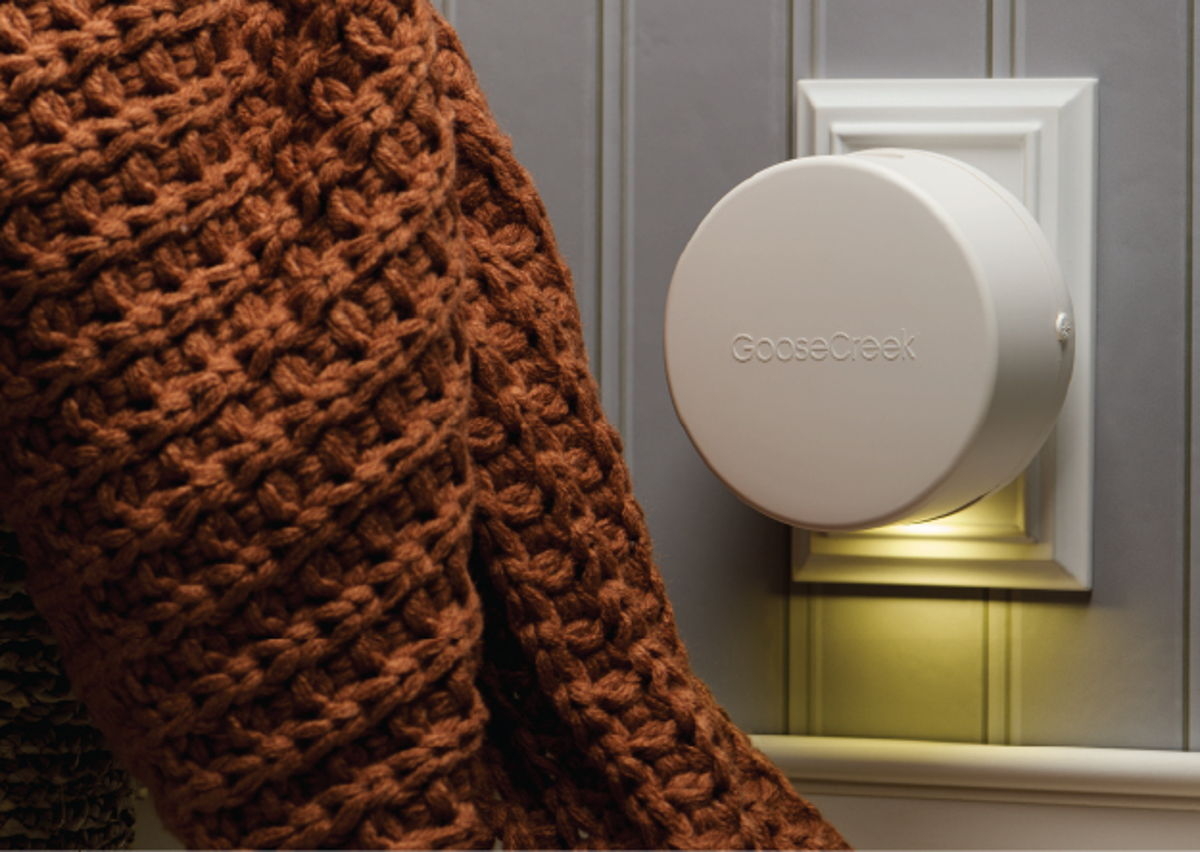 A hand with a knitted sleeve near a wall-mounted device.
